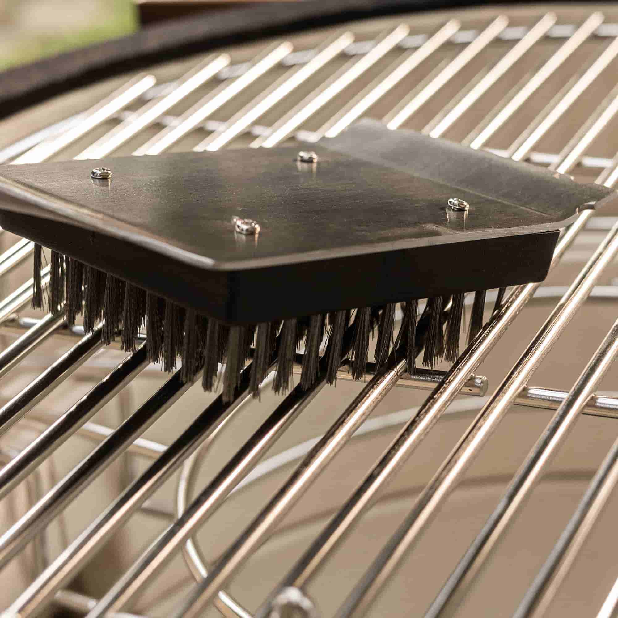 Brosse de nettoyage à poils métalliques posée sur une grille de barbecue en inox.