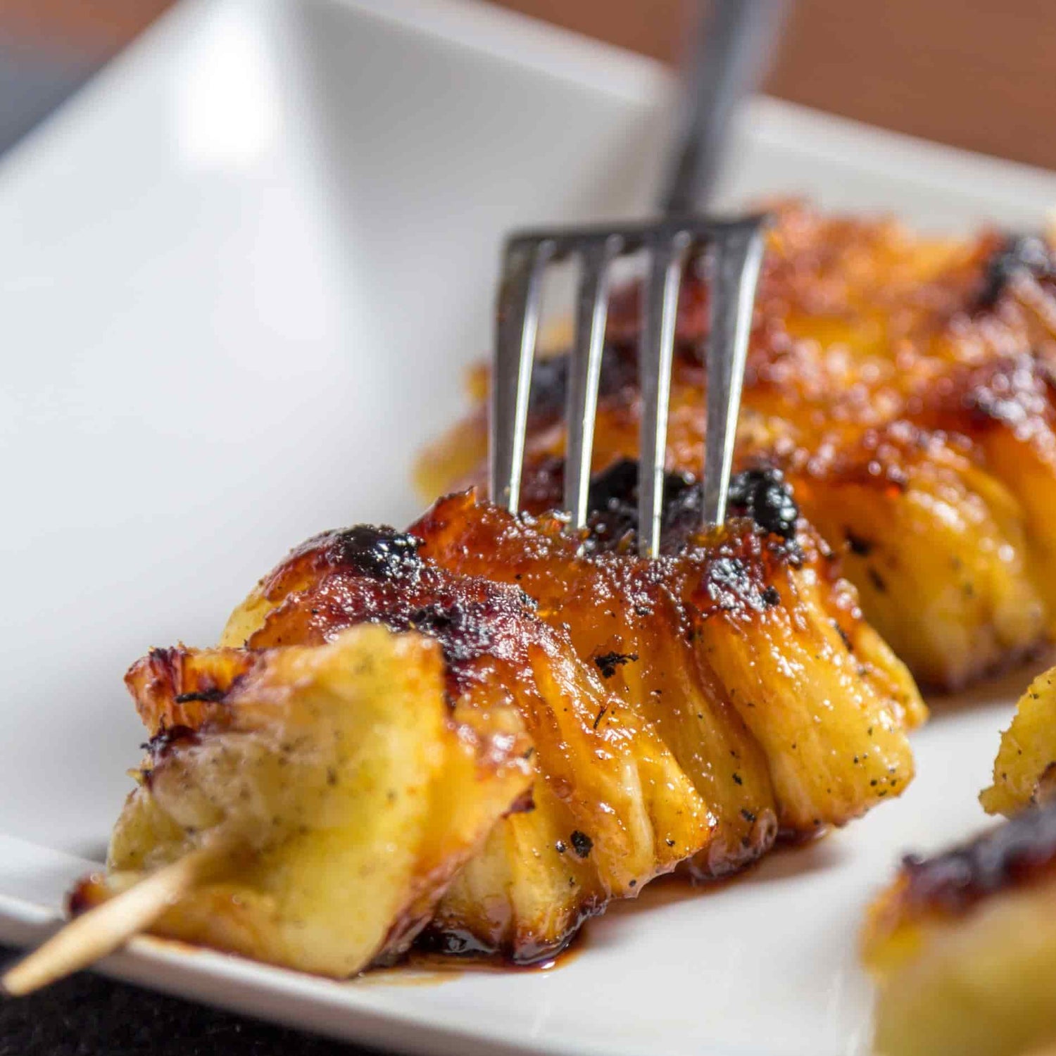 Brochette d’ananas grillé caramélisé cuite au barbecue Kamado Forest Grill, servie sur une assiette blanche.