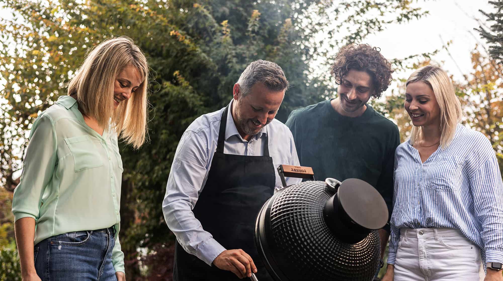 Groupe de personnes profitant d’un moment convivial autour d’un barbecue Kamado Forest Grill dans un jardin.