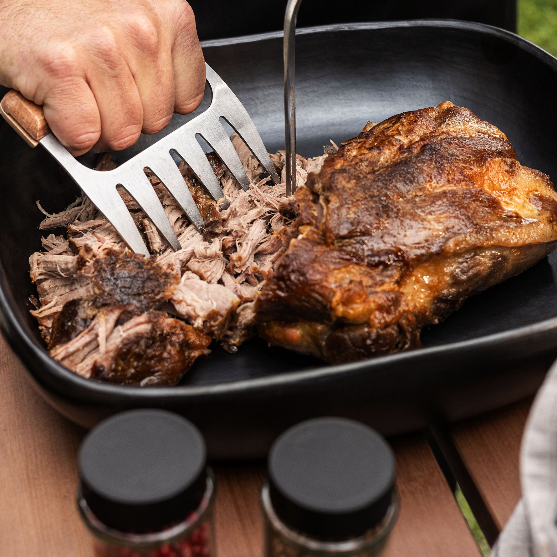 Gros plan sur une viande effilochée à la fourchette dans un plat noir, préparée après cuisson au barbecue Kamado Forest Grill, avec des épices visibles au premier plan.