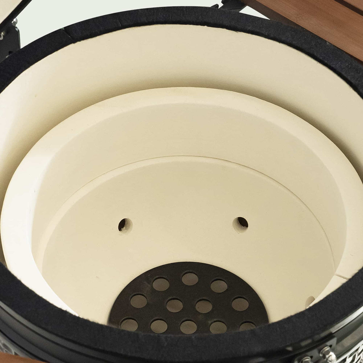 Intérieur d’un barbecue Kamado vide, montrant l’épaisseur de la céramique et la plaque perforée au fond pour une meilleure circulation de l’air et résistance à la chaleur.