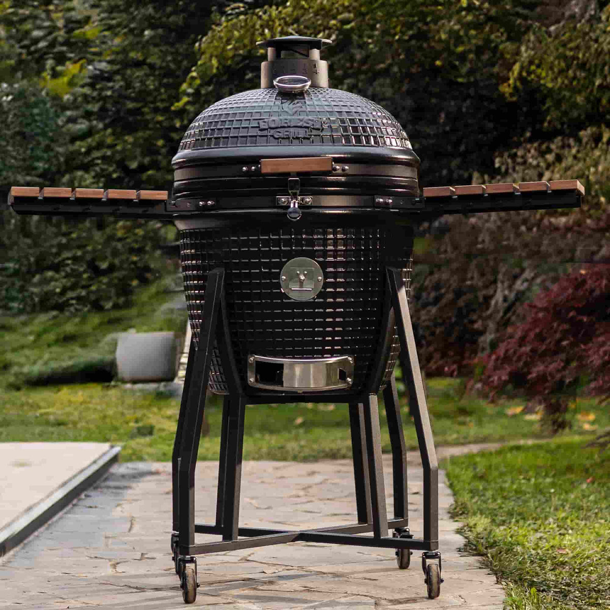 Kamado Forest Grill 22" installé sur son chariot robuste en acier, avec plateaux en bois massif déployés, prêt pour une cuisson en plein air.