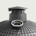 Gros plan sur la cheminée en fonte émaillée d’un barbecue Kamado, avec graduations de réglage de l’air et thermomètre intégré pour un contrôle précis de la température.