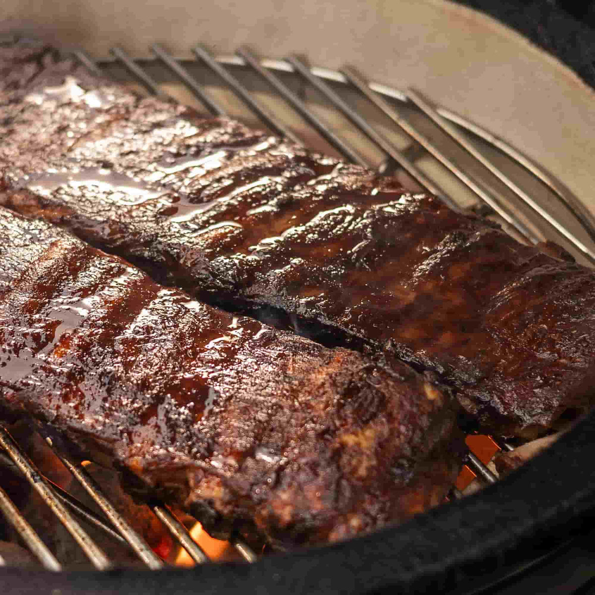 Cuisson de côtes levées caramélisées sur la grille en inox du Kamado Forest Grill, révélant une texture juteuse et un fumage parfaitement maîtrisé.