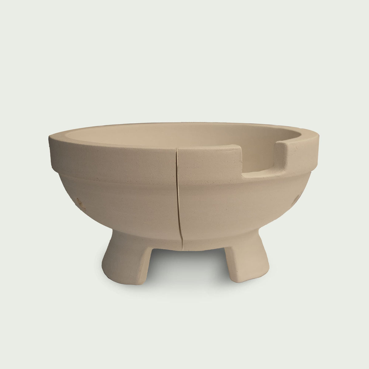 Cuve en céramique beige pour kamado, montrée avec sa séparation centrale et ses encoches supérieures, posée sur trois pieds pour assurer stabilité et circulation de l’air.