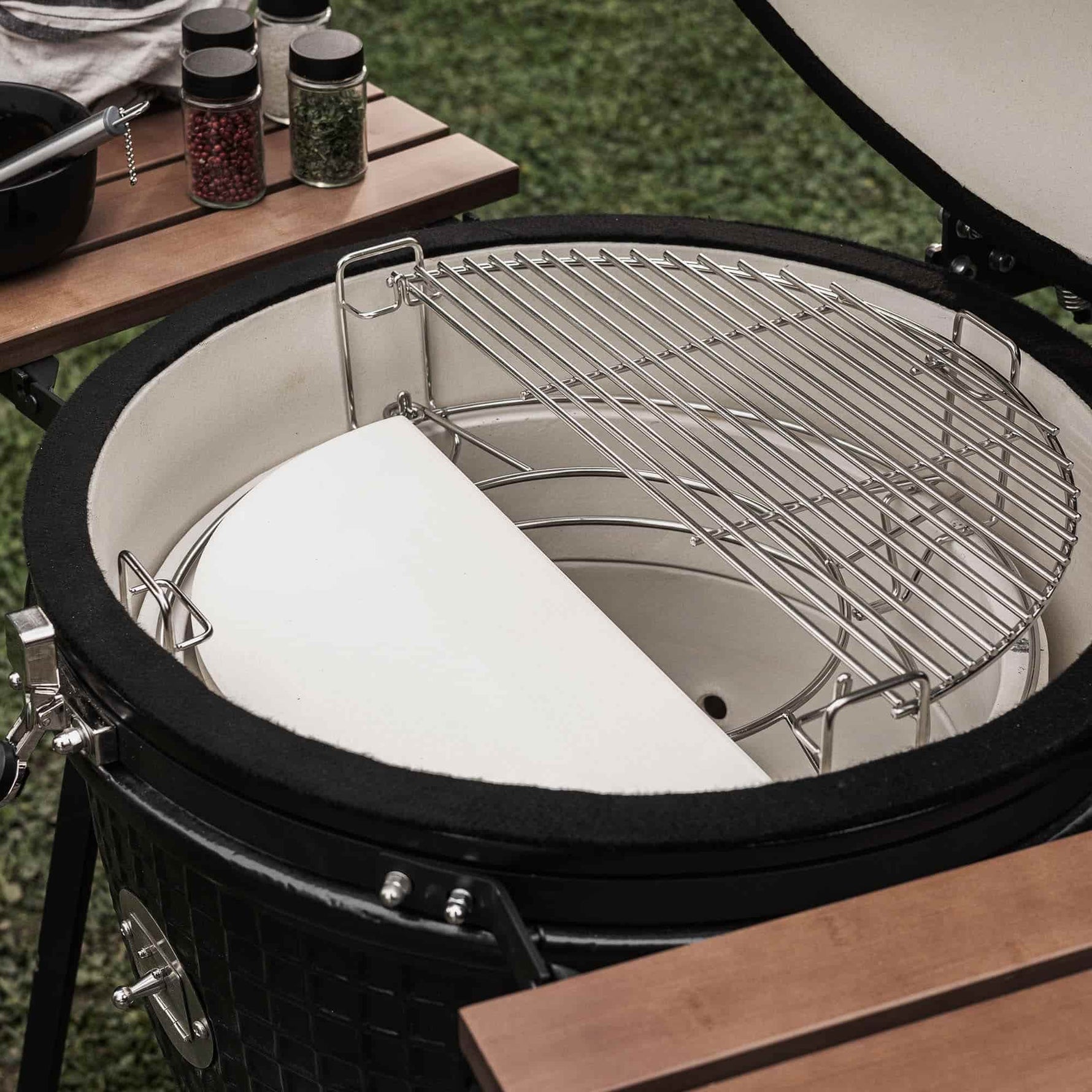 Intérieur d’un barbecue Kamado équipé d’une demi-grille de cuisson en inox et d’une demi-pierre en céramique, permettant une cuisson mixte directe et indirecte.