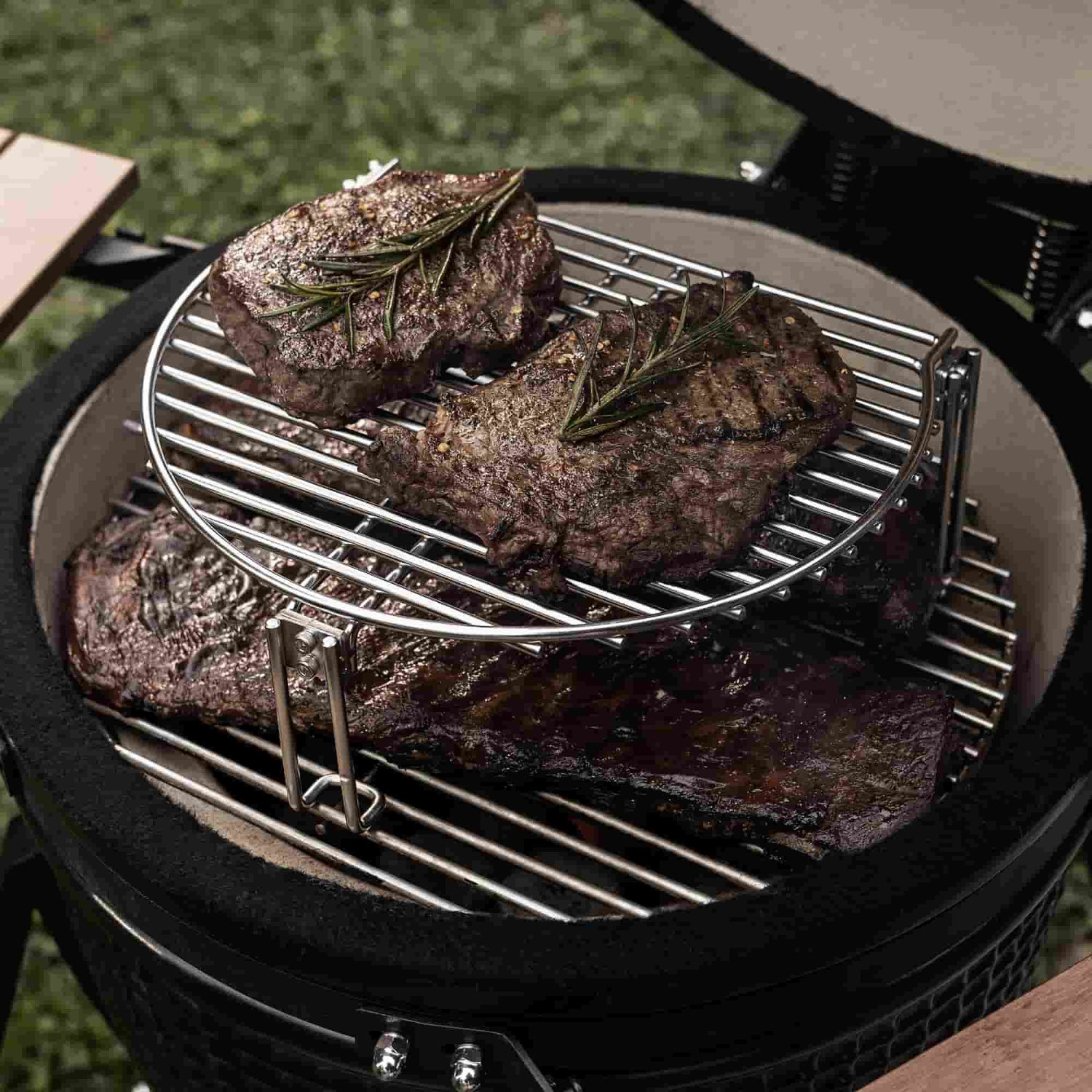 Viande grillée garnie de brins de romarin cuisant sur une grille de cuisson avec extension en inox à deux niveaux à l’intérieur d’un barbecue Kamado.