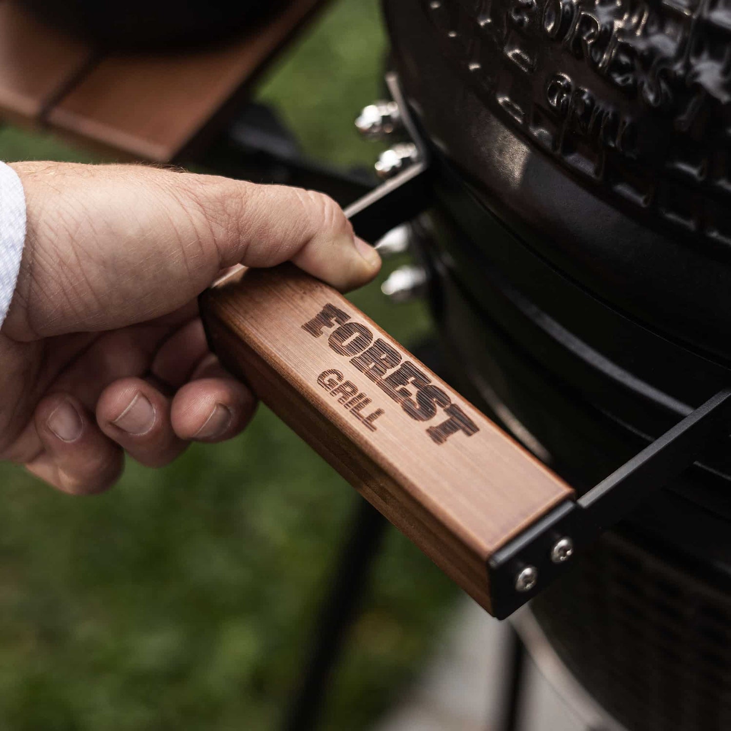 Détail de la poignée en bois gravée Forest Grill sur le barbecue Kamado, illustrant la qualité des finitions.