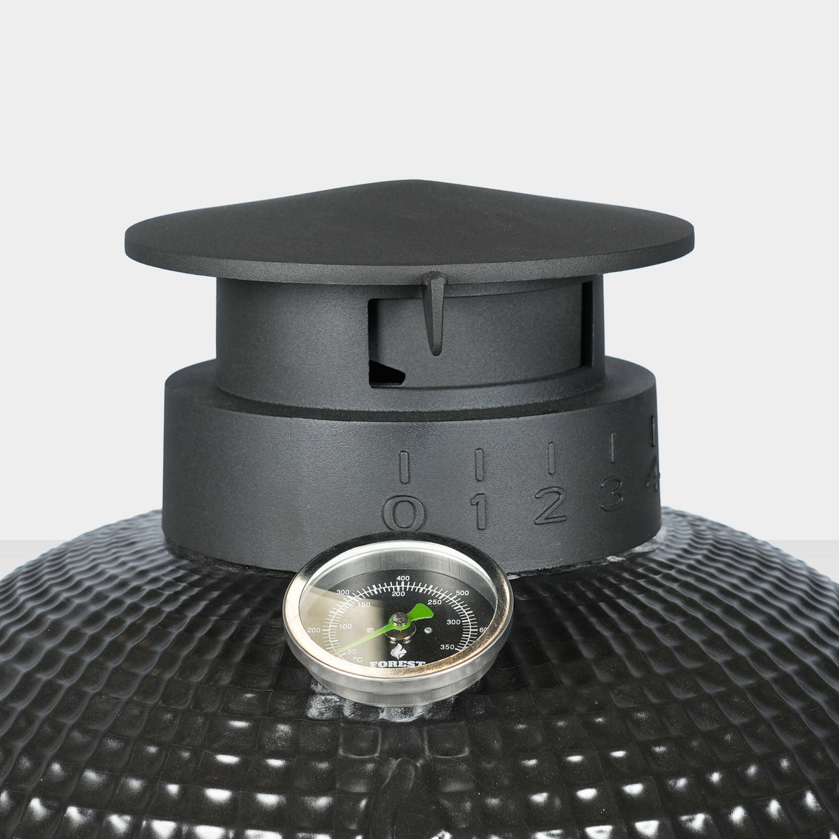 Gros plan sur la cheminée en fonte émaillée d’un barbecue Kamado, avec graduations de réglage de l’air et thermomètre intégré pour un contrôle précis de la température.