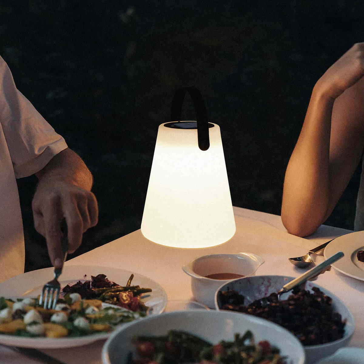 Lampe Cône Forest Grill éclairant une table dressée pour un dîner en extérieur, créant une atmosphère chaleureuse et intime grâce à sa lumière douce et diffuse.