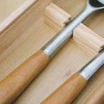 Gros plan sur les manches en bois et acier inoxydable d’ustensiles de barbecue,  rangés dans un coffret en bois.