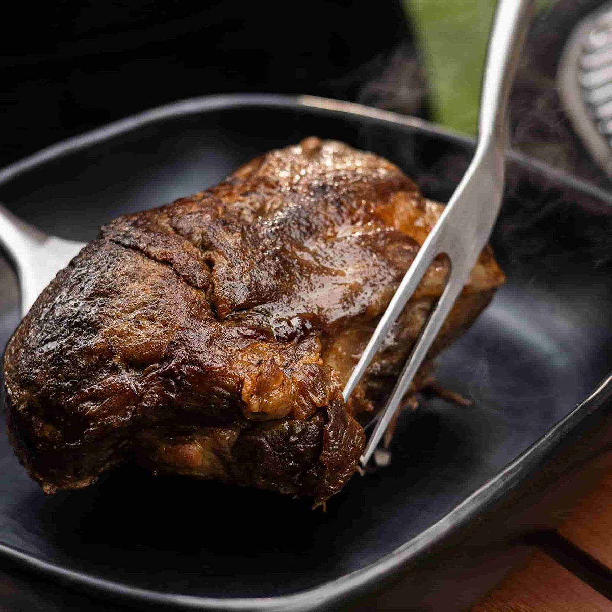 Morceau de viande grillée juteuse maintenu avec une fourchette de barbecue en acier inoxydable, dégageant encore de la vapeur.