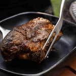 Morceau de viande grillée juteuse maintenu avec une fourchette de barbecue en acier inoxydable, dégageant encore de la vapeur.