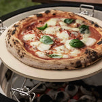 Pizza cuite au feu de bois sur une pierre à pizza dans un barbecue kamado, avec une pâte dorée, du fromage fondant et des feuilles de basilic frais.