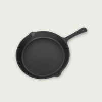Black cast iron pan seen from above with long molded handle, shown in profile on a light background, ideal for even cooking of meats, vegetables, or dishes on the Kamado.