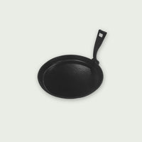 Black cast iron pan with molded handle, presented on a light background, ideal for searing, gratinating, or serving dishes directly from the barbecue or the Kamado.