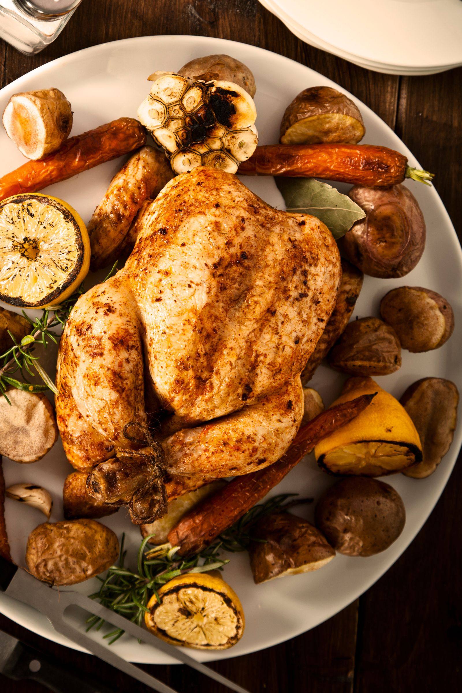 Poulet rôti au kamado doré accompagné de légumes caramélisés, de pommes de terre et de citrons grillés.