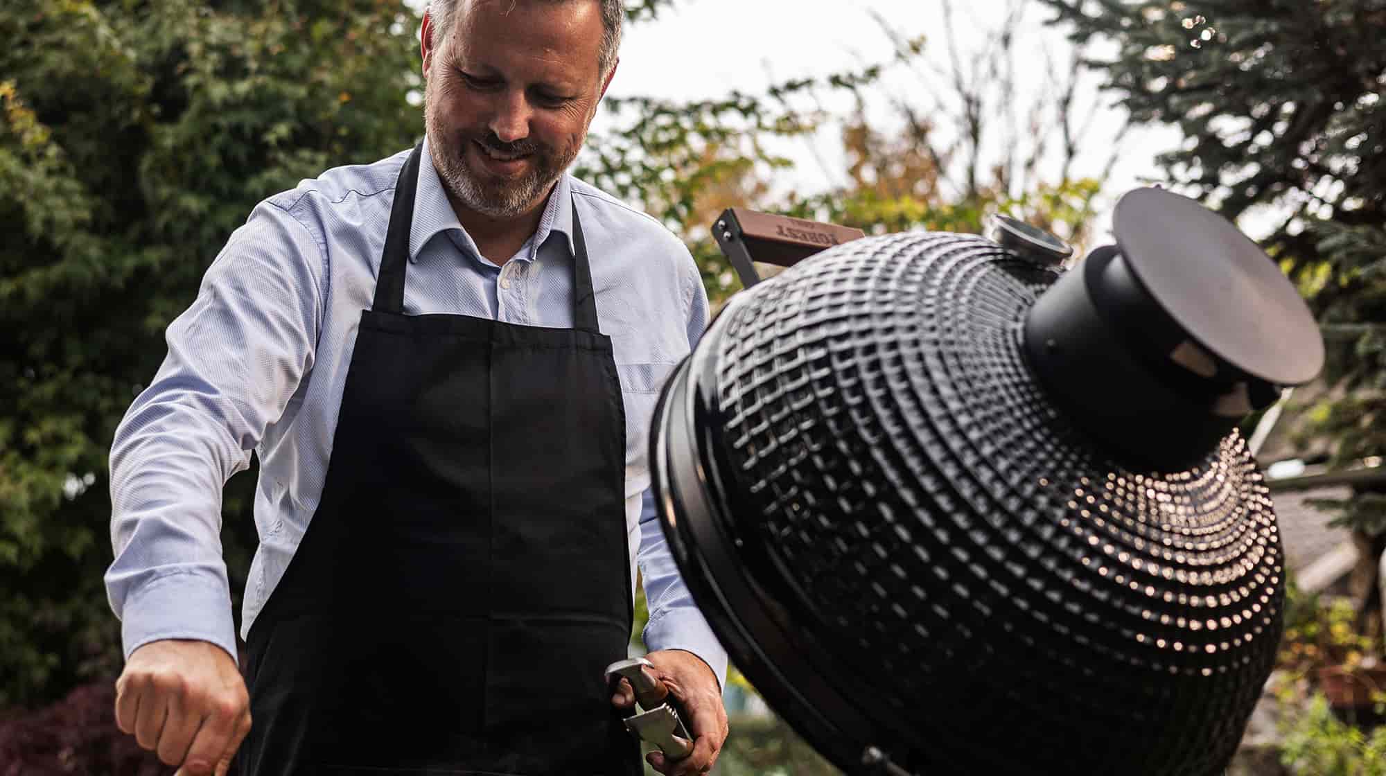 Personne cuisinant au barbecue Kamado Forest Grill dans un jardin, illustrant la qualité et la convivialité de la cuisson au charbon.