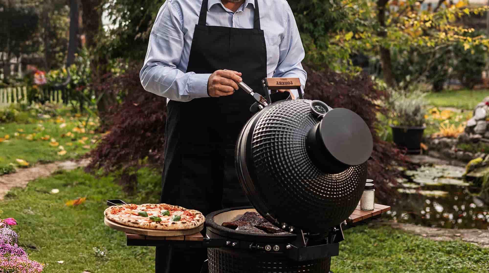 Personne utilisant pour la première fois un barbecue Kamado Forest Grill dans un jardin, avec une pizza et des grillades en préparation.