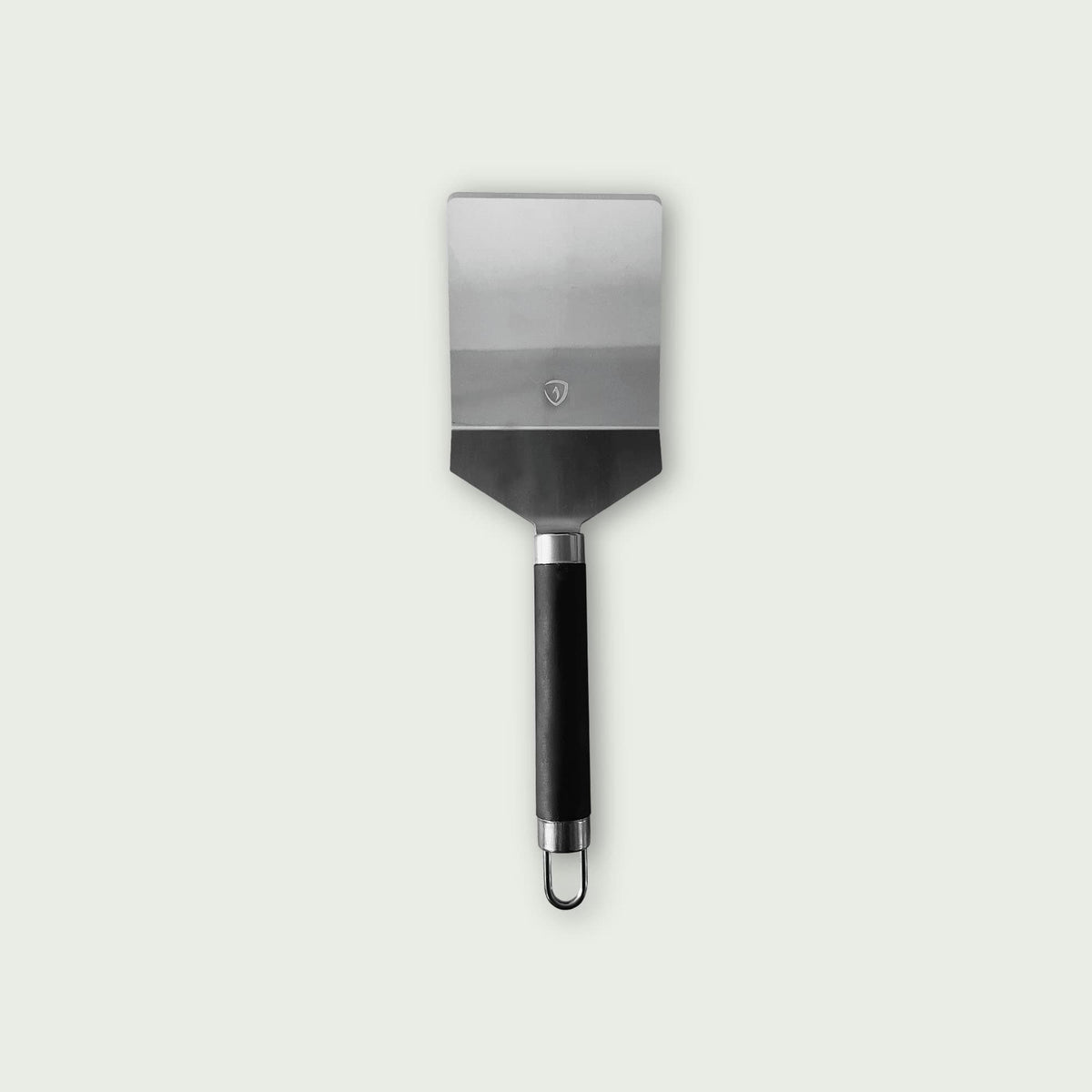 Spatule classique en acier inoxydable avec manche noir ergonomique et anneau de suspension, conçue pour une utilisation sur plancha ou barbecue.