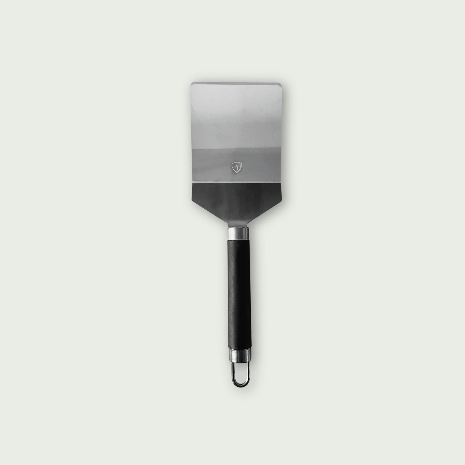 Spatule classique en acier inoxydable avec manche noir ergonomique et anneau de suspension, conçue pour une utilisation sur plancha ou barbecue.