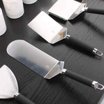 Ensemble de spatules en acier inoxydable avec manches noirs, disposées sur une table en bois foncé.